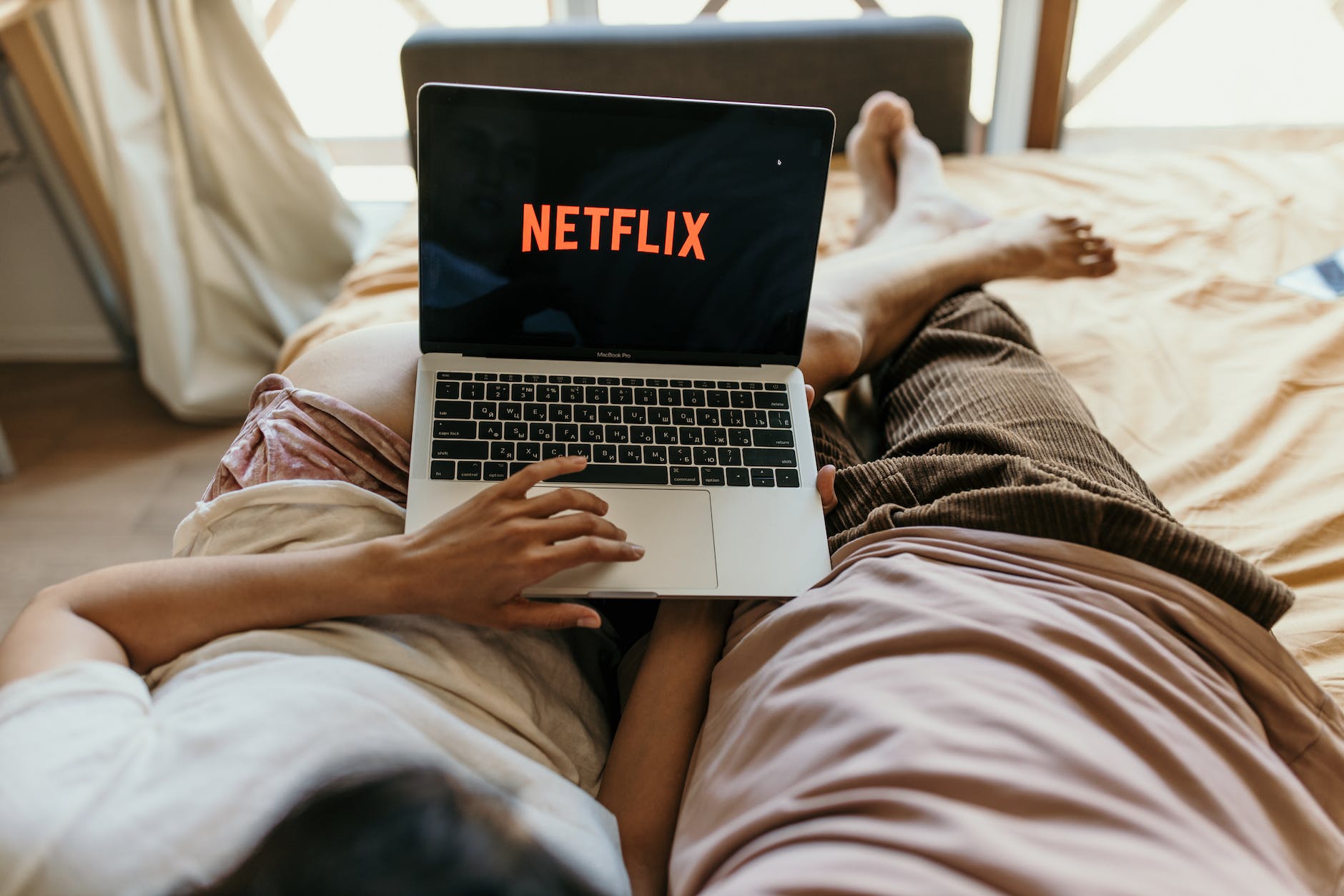 a couple lying on bed watching netflix on a laptop